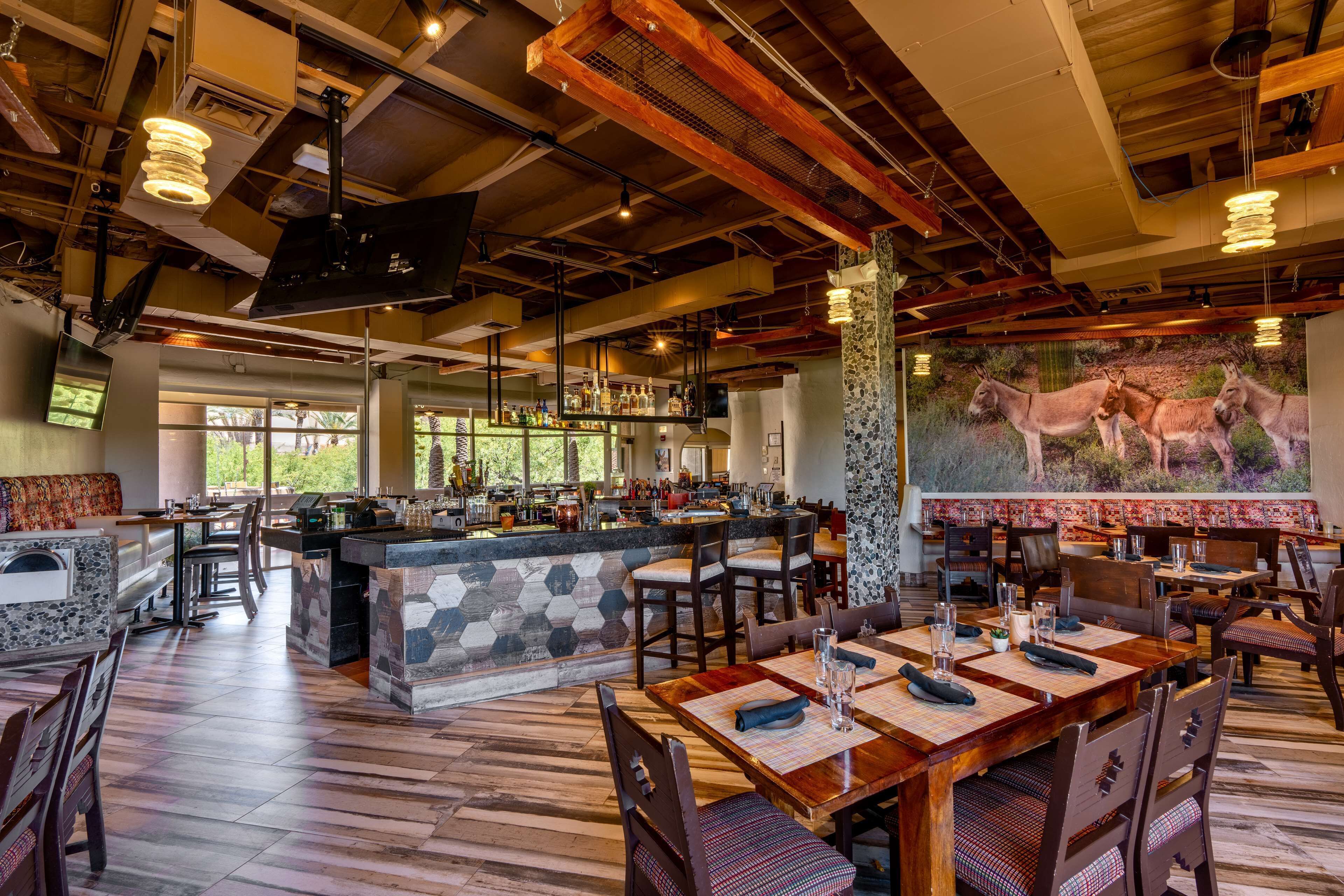 Un restaurante con zona de bar, suelo de madera y un mural de burros en la pared.