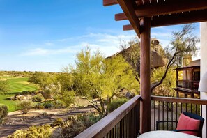 A balcony with a view of a golf course, a wooden pergola, and a chair with a cushion.