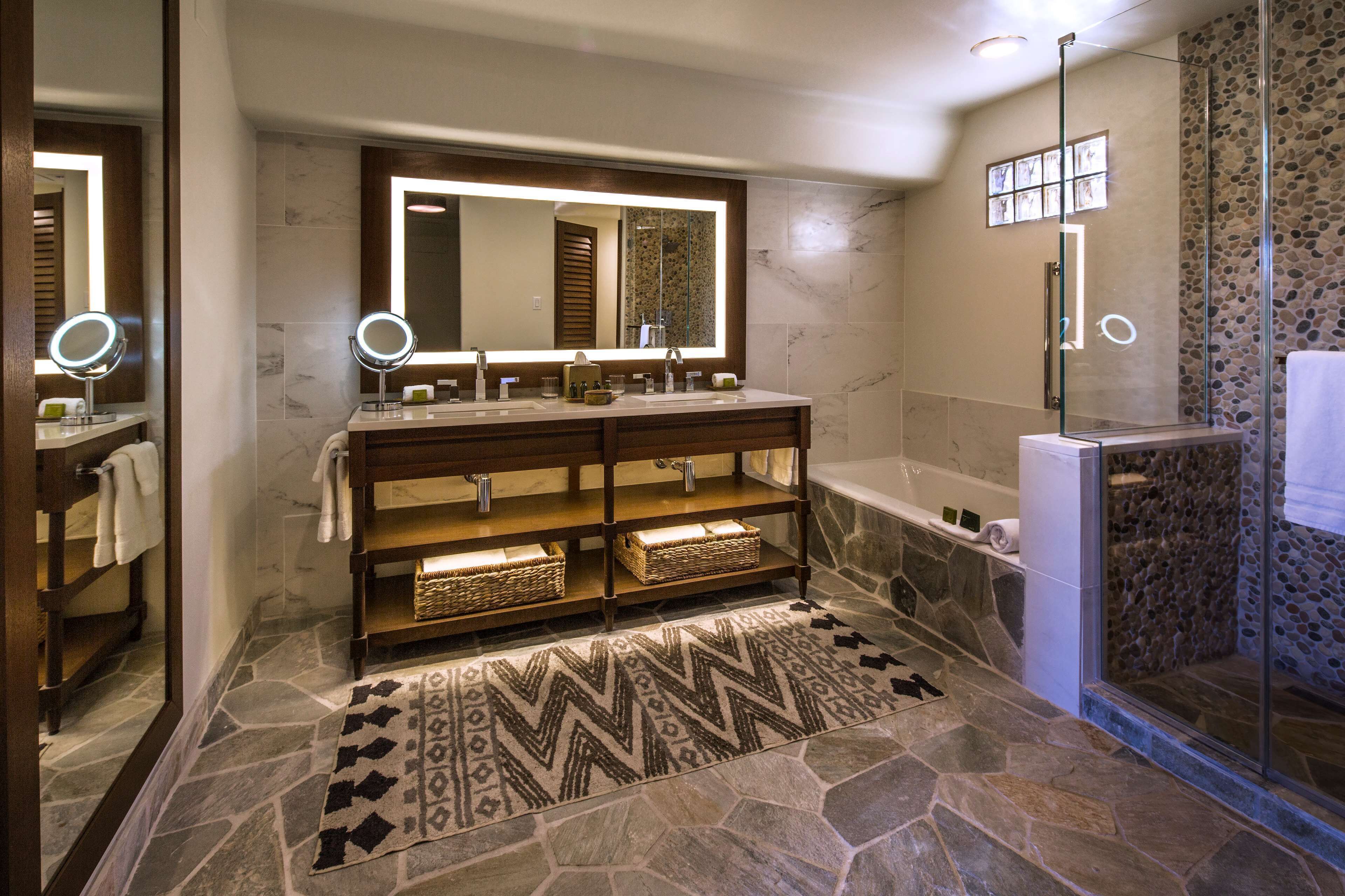 A modern bathroom with a stone floor, a large mirror, a bathtub, and a shower area.