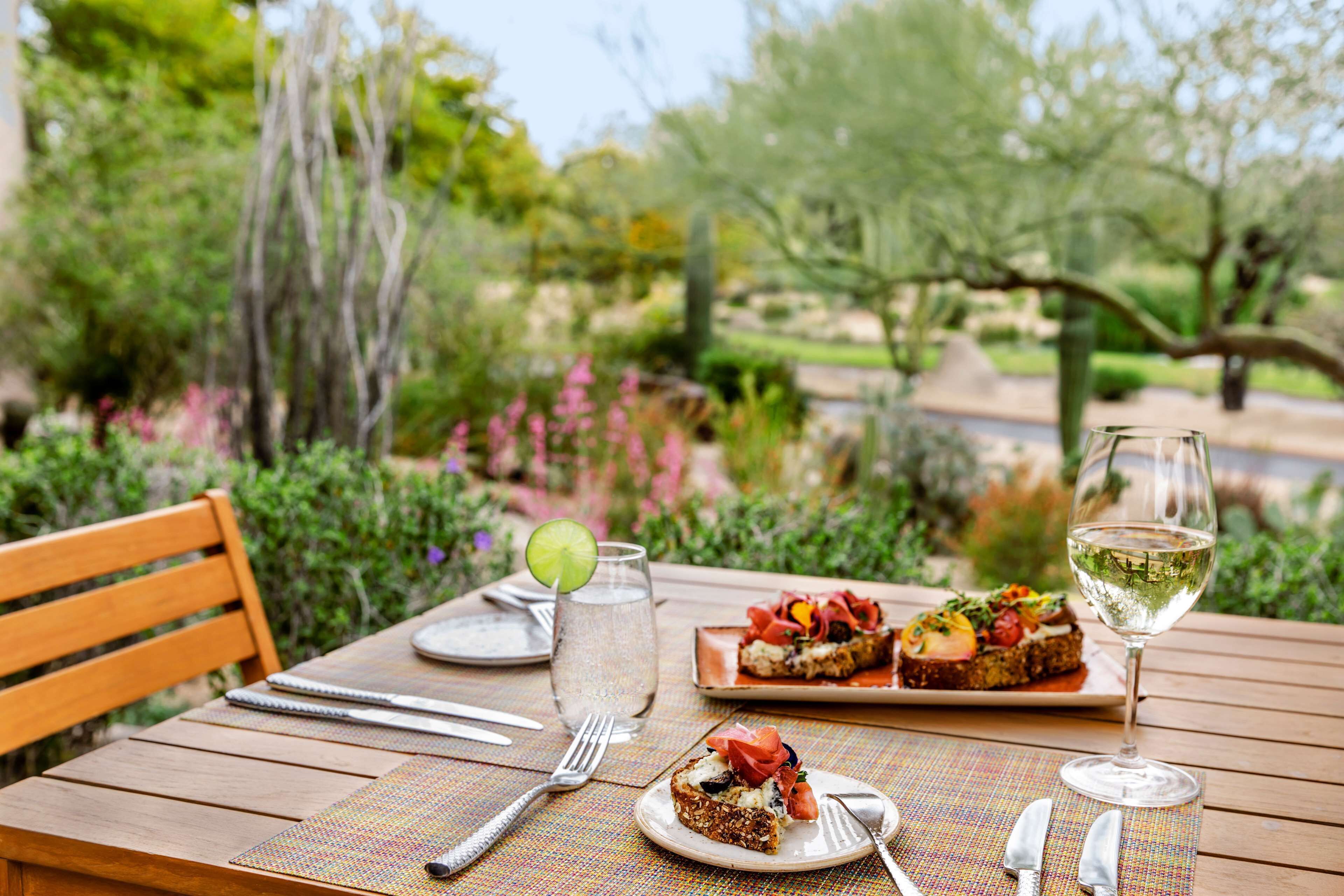 A wooden table set with plates, cutlery, a glass of water, a glass of white wine, and a notebook.