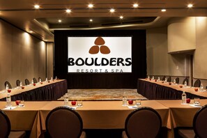 A conference room at Boulders Resort & Spa with a long table, chairs, and a large screen displaying the resort's logo.