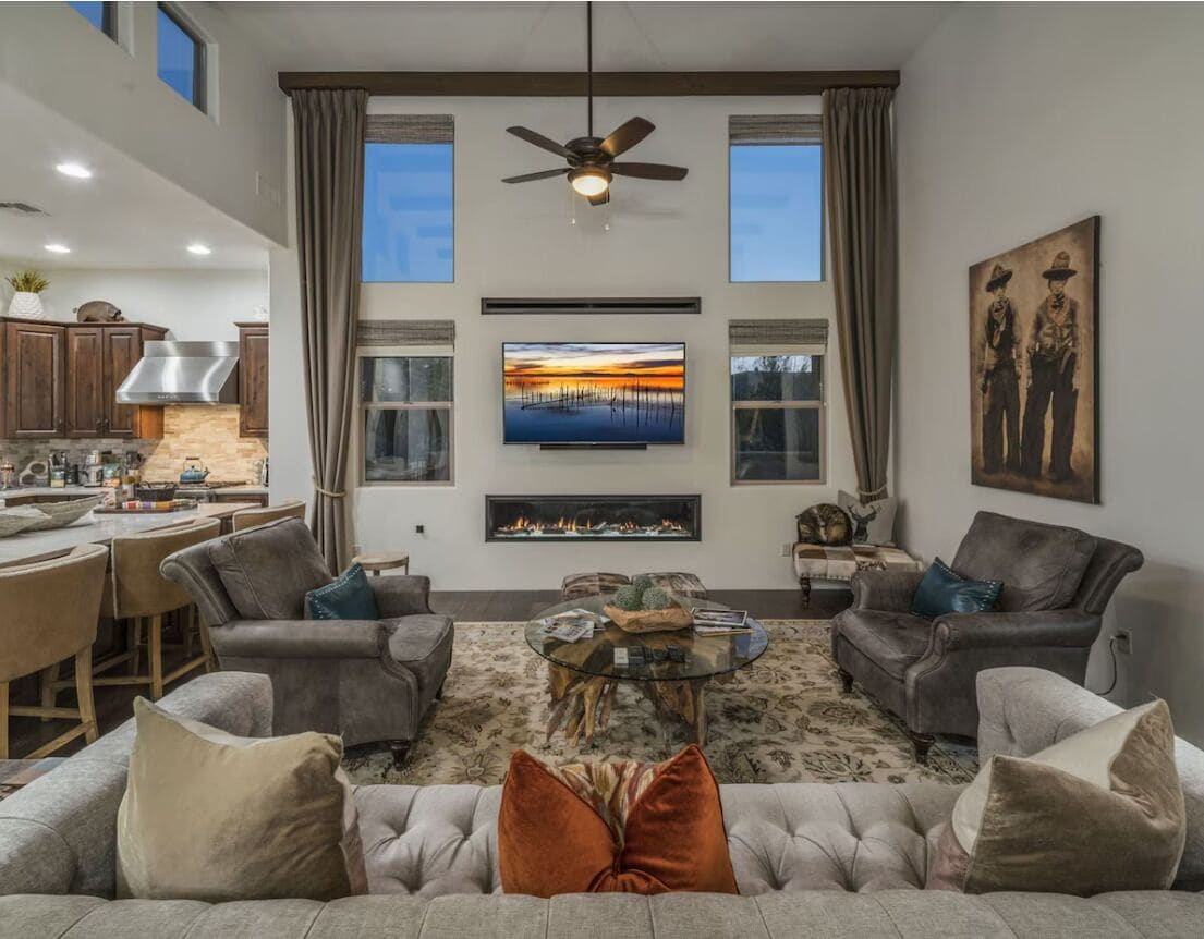 A spacious living room with a fireplace, a television, and a dining area with a kitchen in the background.