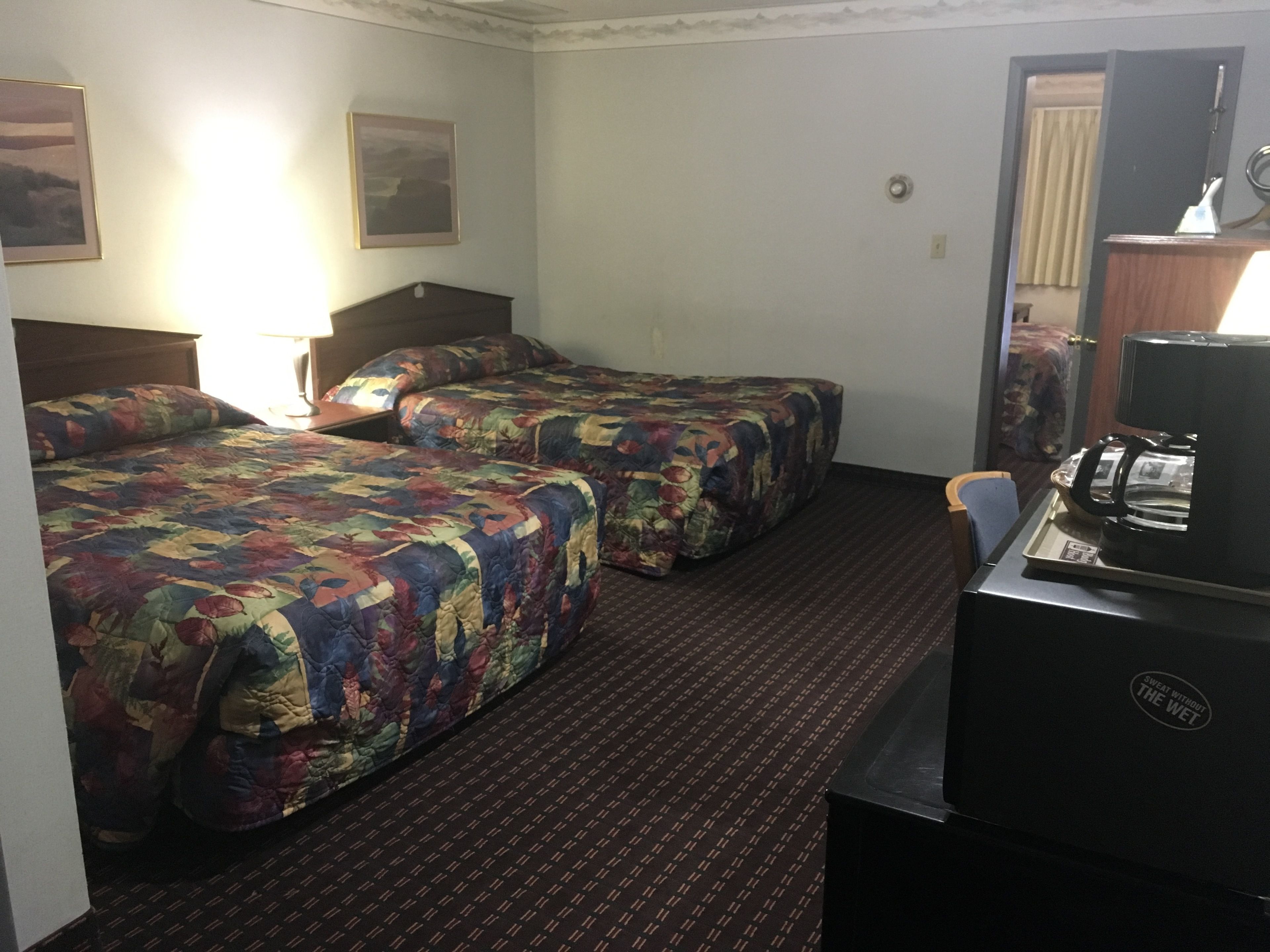 A hotel room with two beds, a desk with a coffee maker, and a mirror.