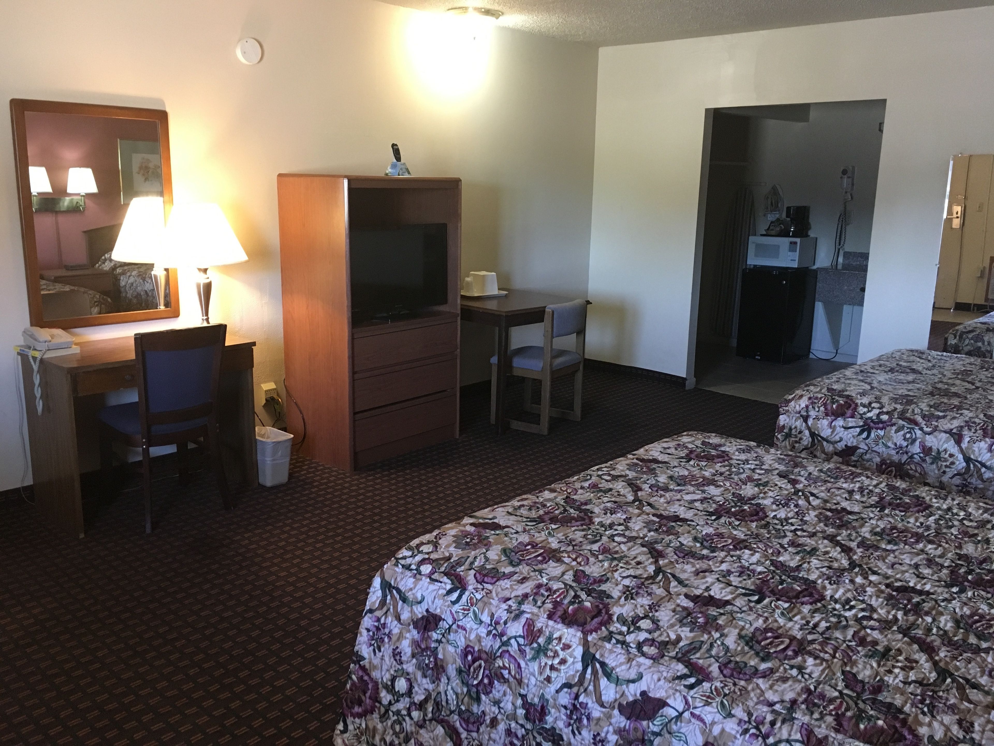 A hotel room with a desk, chair, television, and two beds with floral bedding.