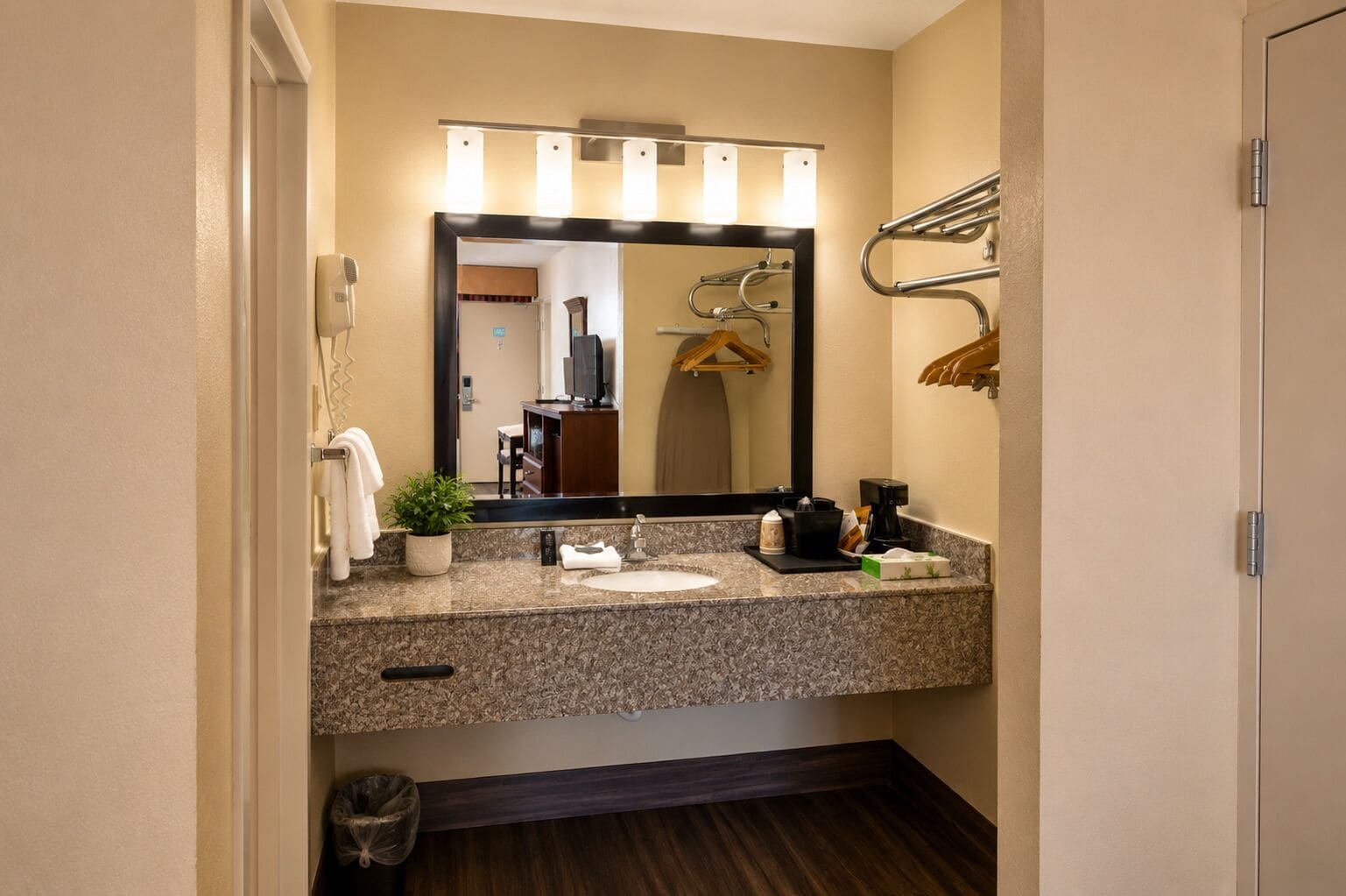 Un baño con encimera de granito, un lavabo, un espejo y un perchero para toallas.