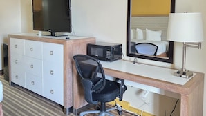 Habitación de hotel con escritorio, televisor, microondas, silla, cómoda y espejo.