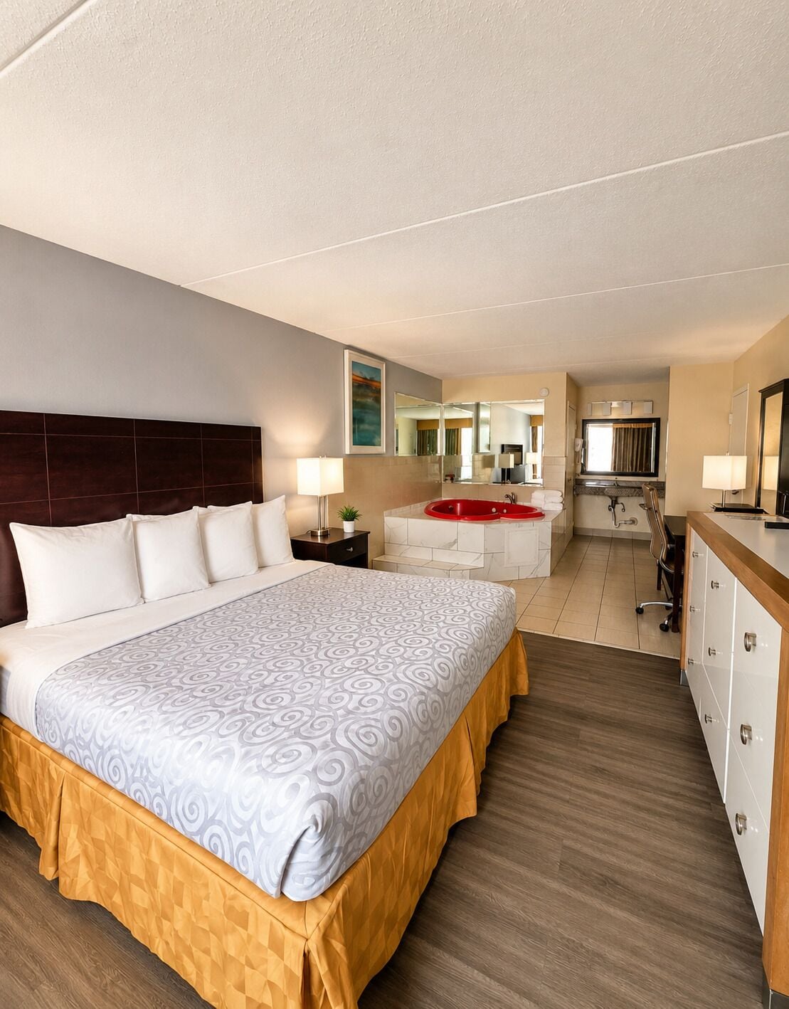 A hotel room with a large bed, a bathroom with a red bathtub, and a kitchenette.