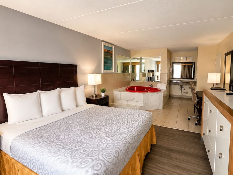 A hotel room with a large bed, a bathroom with a red bathtub, and a kitchenette.