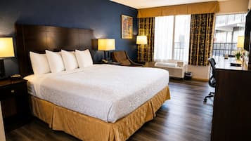 Habitación de hotel con una cama grande, dos mesitas de noche, un escritorio, una silla, un ventanal con cortinas y un cuadro en la pared.