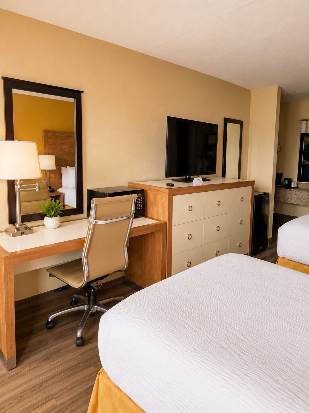 A hotel room with a bed, a desk with a computer, a television, a mirror, and a dresser.
