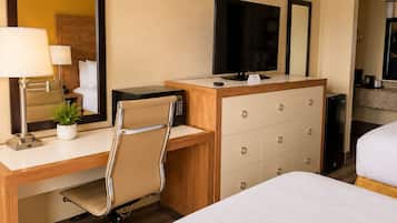A hotel room with a bed, a desk with a computer, a television, a mirror, and a dresser.