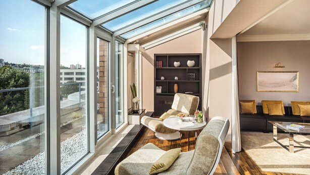 Una sala de estar moderna con techo de vidrio, un conjunto de sofás, una mesa de centro y una estantería.