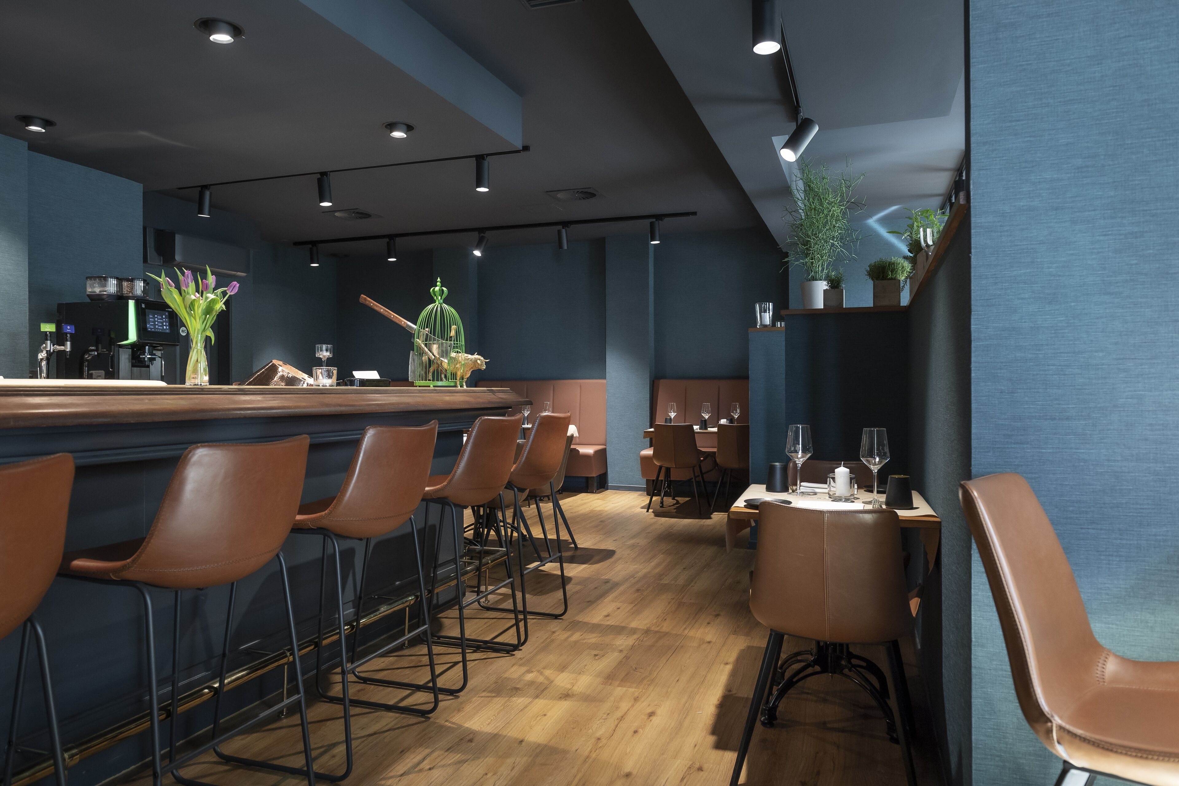 A modern bar area with wooden flooring, bar stools, and a counter with a coffee machine.