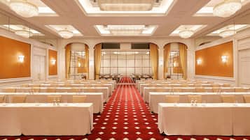 A conference room with rows of tables, chandeliers, and a red carpeted floor.