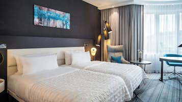 A hotel room with a large bed, a desk, a chair, a lamp, and a painting on the wall.