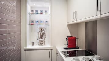 Una cocina compacta con una cafetera expreso integrada, una máquina de café y un hervidor de agua sobre una encimera blanca.