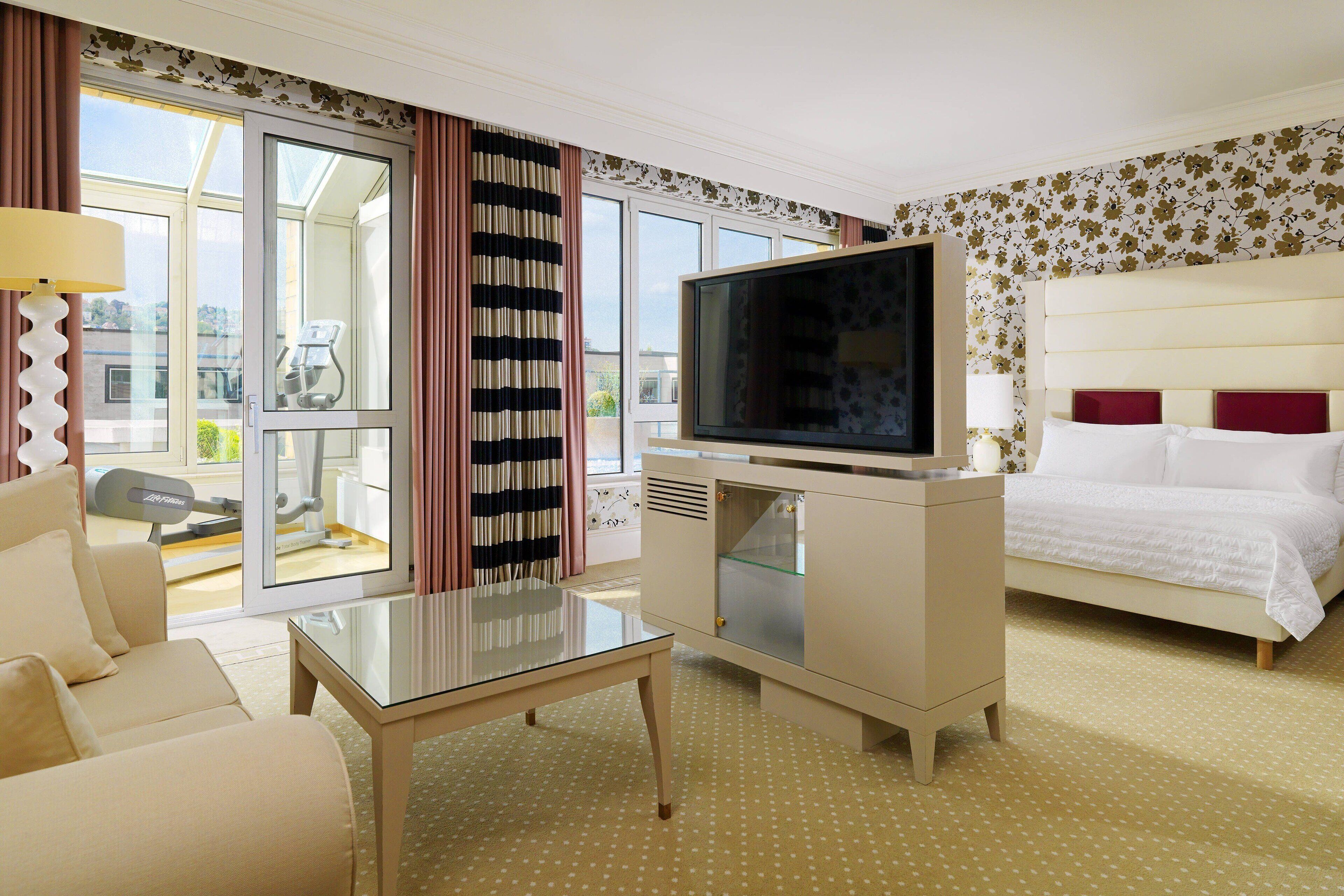 Ein Hotelzimmer mit Bett, Fernseher, Sofa, Glastisch und Blick nach draußen.