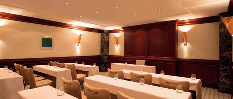 A conference room with multiple tables and chairs, equipped with table lamps and recessed ceiling lights.
