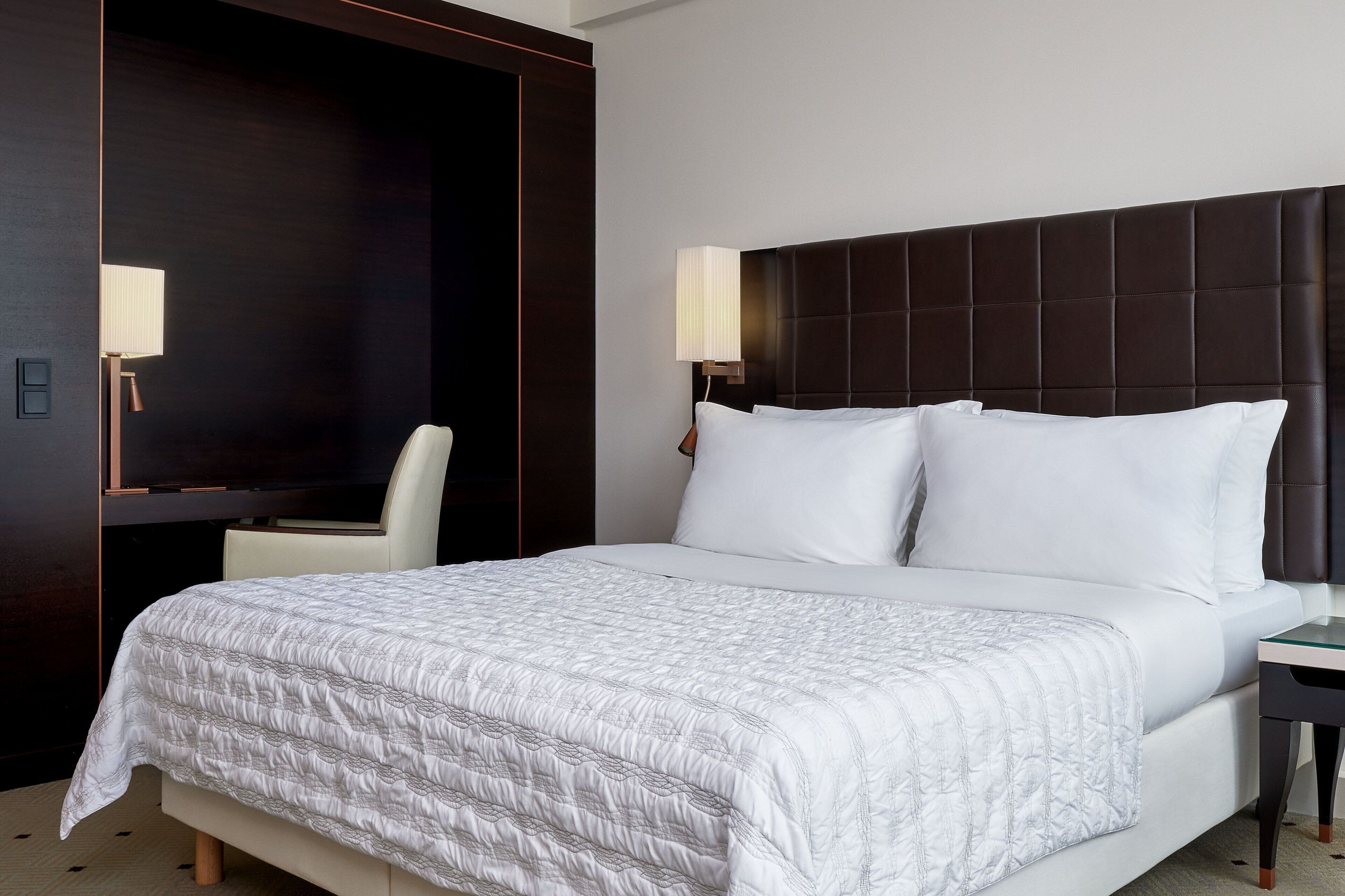 Ein Hotelzimmer mit einem großen Bett, einem dunklen Kopfteil, einem Nachttisch und einem Sessel.