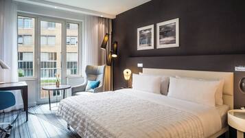 Habitación de hotel con una cama grande, un escritorio, una silla, una lámpara y vistas al exterior.