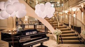 A grand piano with "MR & MRS" on a cushion, a staircase with golden railings, and white balloons.