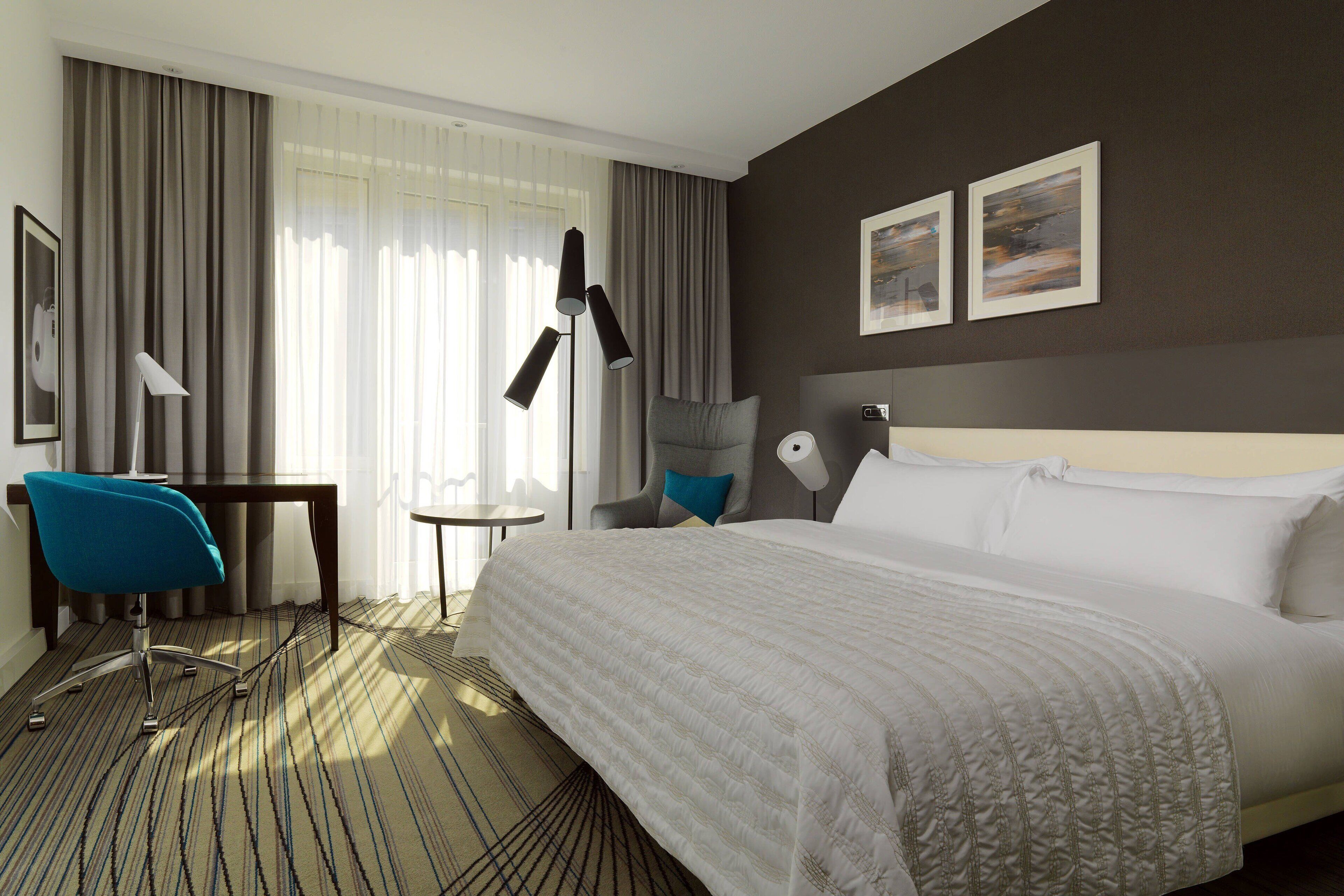 Una habitación de hotel con una cama grande, un escritorio, una silla y una lámpara.
