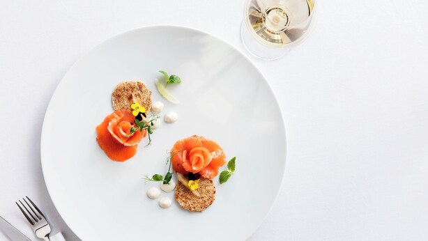 A white plate with two pieces of food, a fork, and a glass of white wine on a white table. - Le Méridien Stuttgart (Stuttgart)