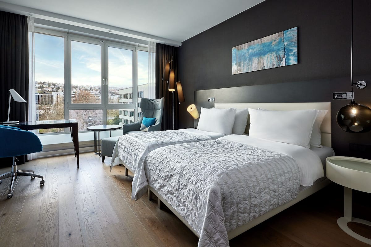A hotel room with a large bed, a desk, a chair, and a view of the city.