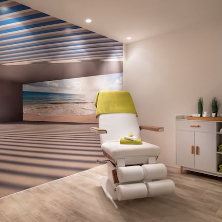A modern spa room with a relaxation chair, a massage table, and a cabinet with towels.
