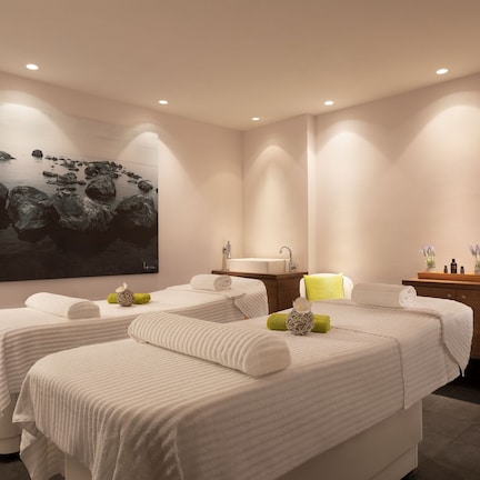 A spa room with two beds, a sink, and a large painting of rocks.