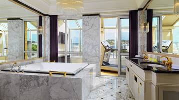 A luxurious bathroom with a large marble bathtub, a separate sink, and a treadmill in the background.