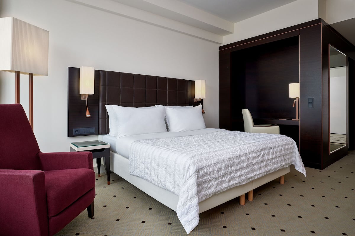 A hotel room with a large bed, a red armchair, a desk, and a mirror.