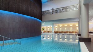 Una piscina interior moderna con techo alto y un área de estar con sillas y mesas.
