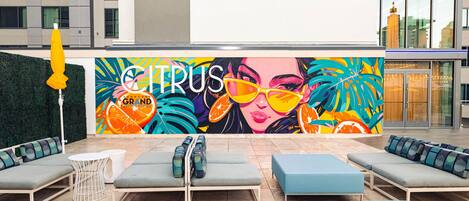 A rooftop lounge area with outdoor seating, a mural, and a view of the cityscape.