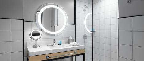A modern bathroom with a vanity, two illuminated mirrors, a sink, and a glass-enclosed shower area.
