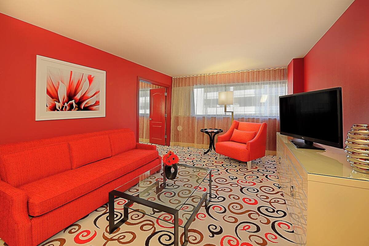 Um quarto com um sofá vermelho, uma poltrona vermelha, uma televisão e um tapete estampado.