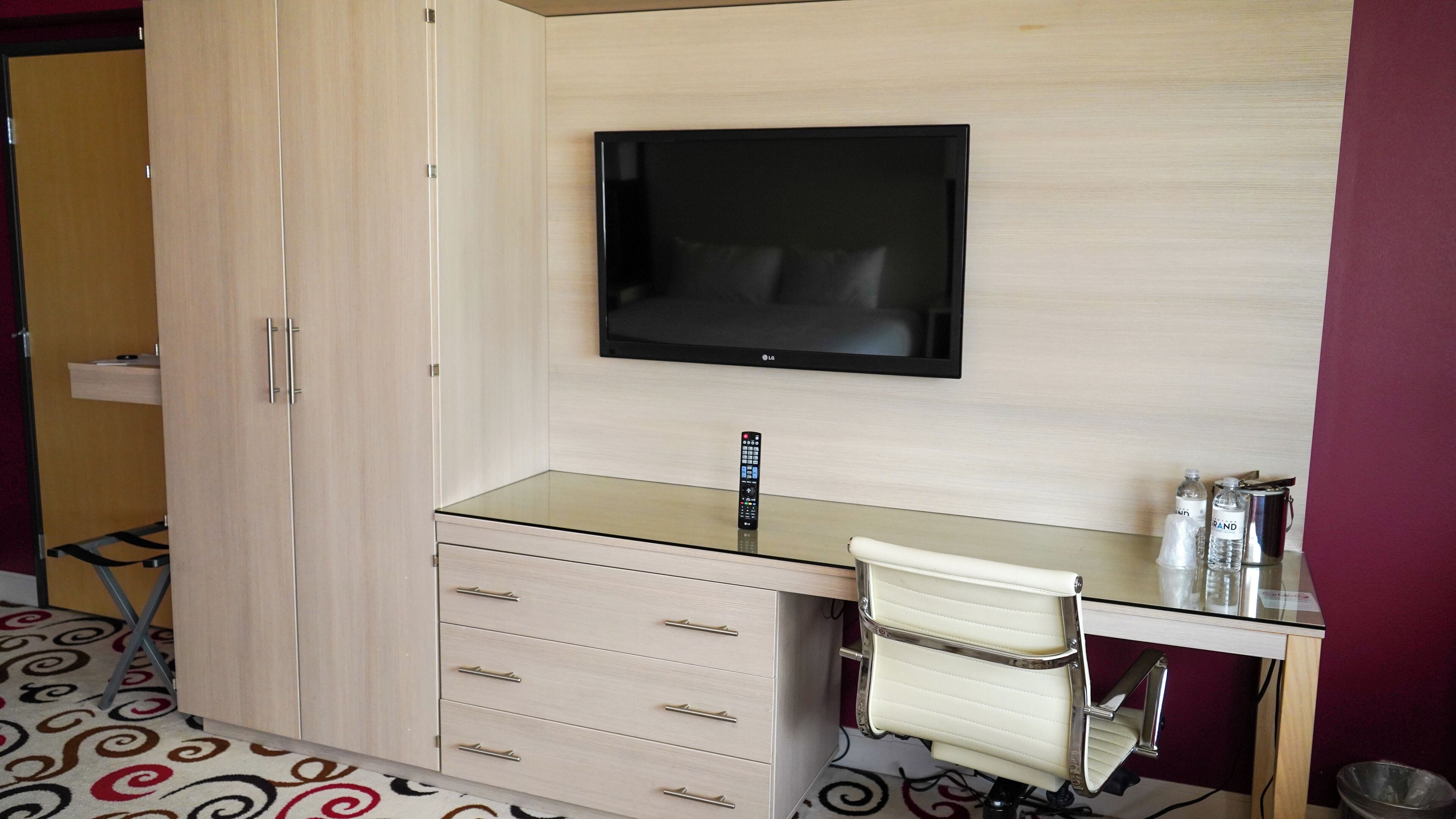 A hotel room with a bed, a desk with a chair, a TV, and a minibar.