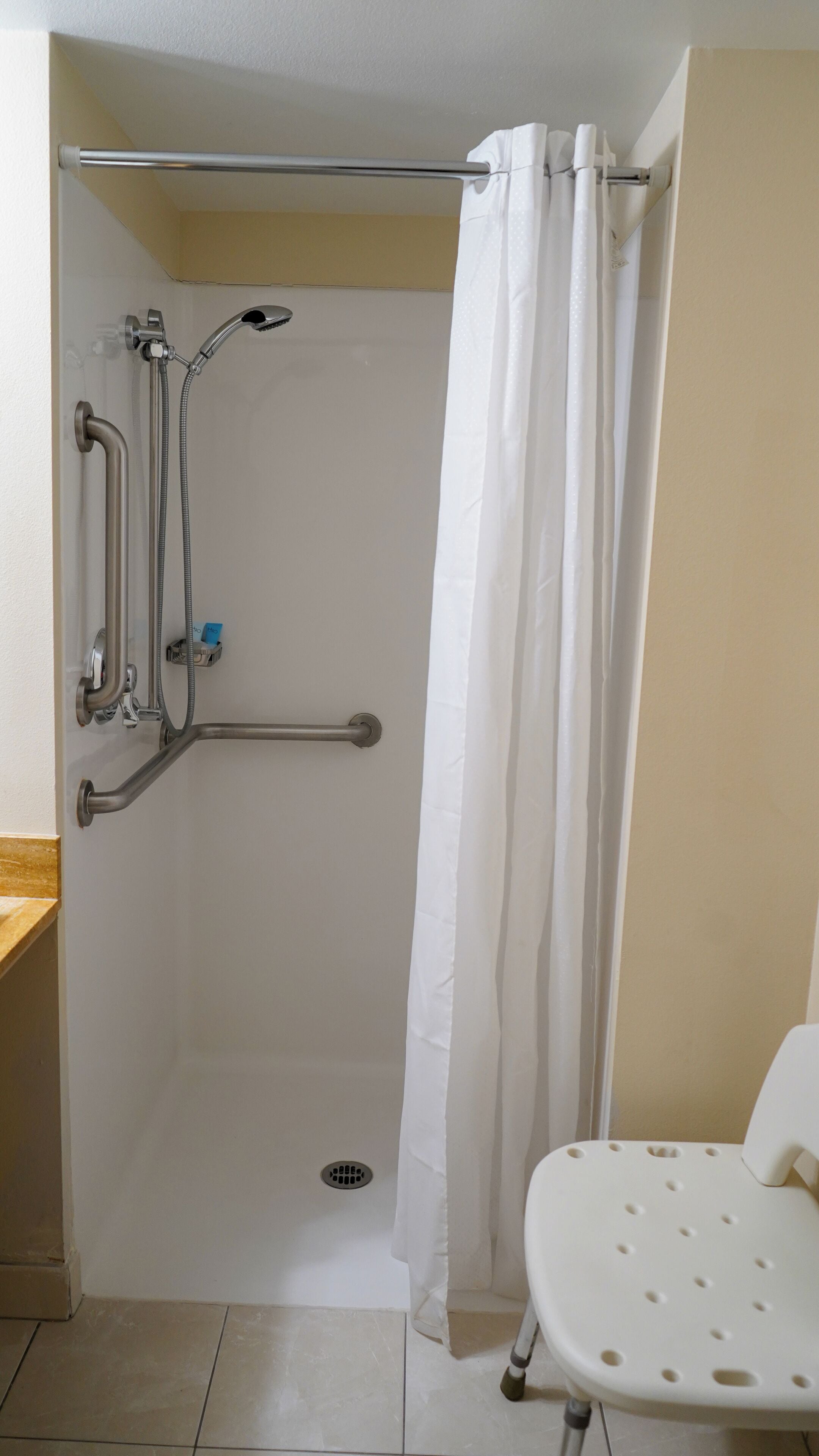 Un espace douche équipé d’une barre d’appui, d’un pommeau de douche à main et d’un rideau blanc.