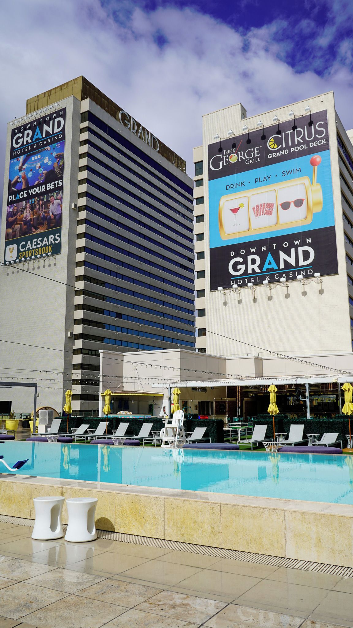 A hotel with a pool area, multiple lounge chairs, and a large billboard advertising a casino.