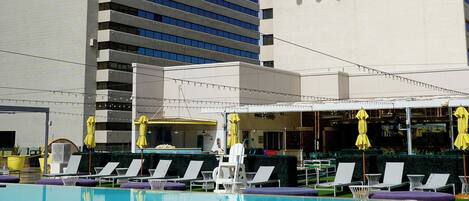 A hotel with a pool area, multiple lounge chairs, and a large billboard advertising a casino.
