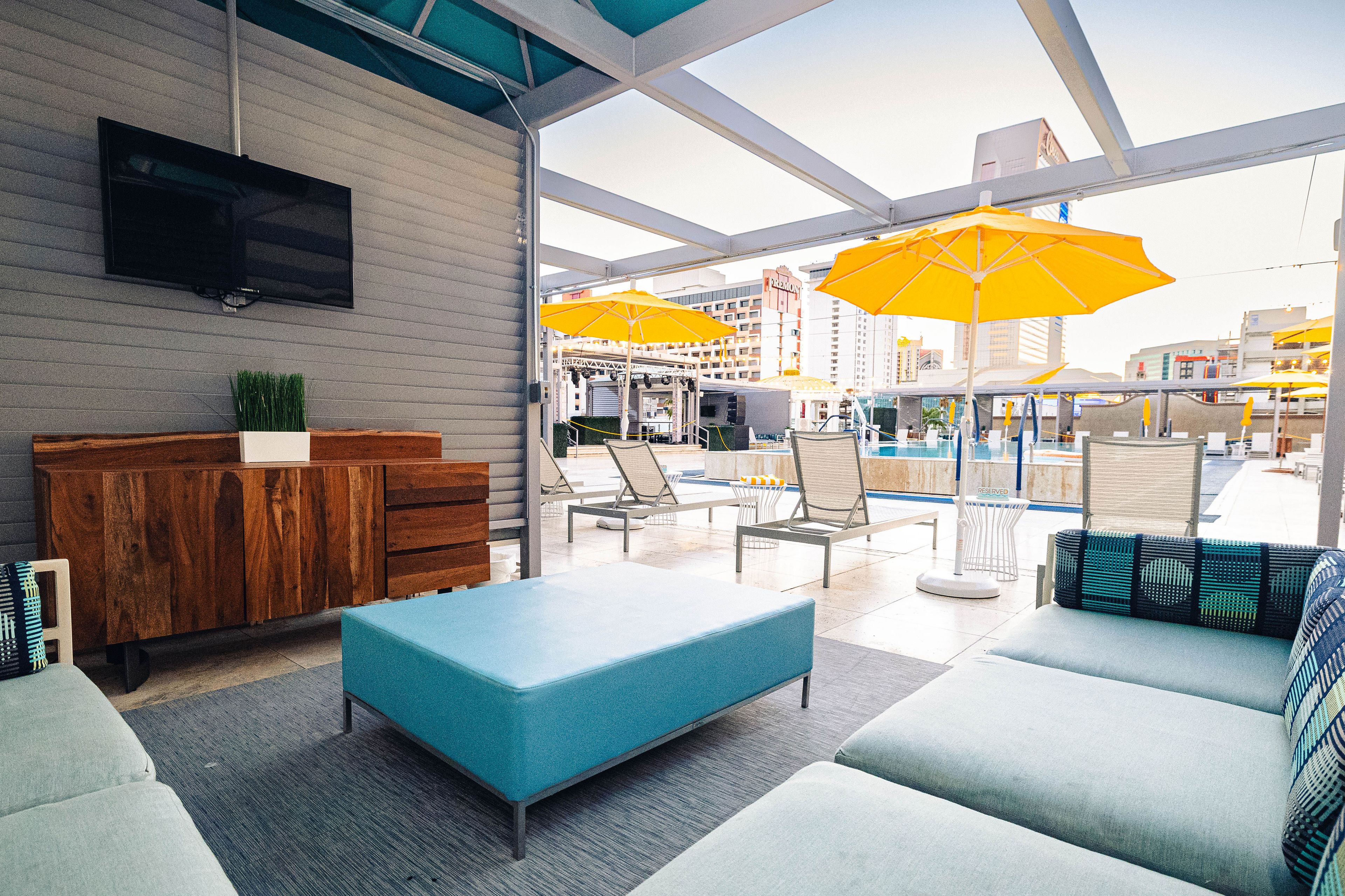 A modern lounge area with a flat-screen TV, wooden furniture, and outdoor seating with yellow umbrellas.