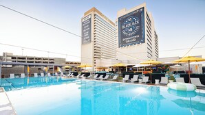 Uma área de piscina com espreguiçadeiras e guarda-sóis, um grande anúncio de Black Jack, e uma garagem de estacionamento ao fundo.