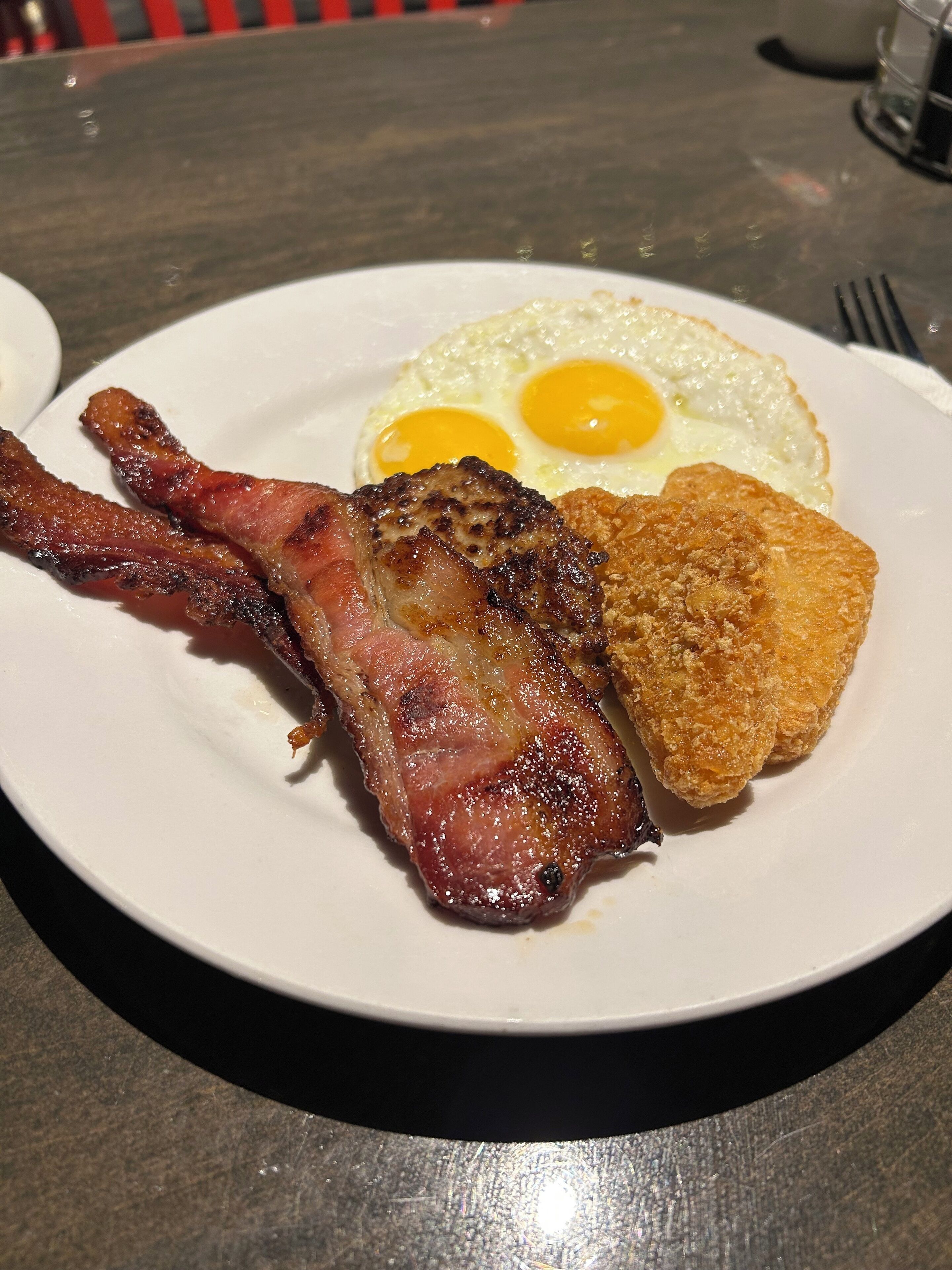 A breakfast plate with bacon, fried eggs, and a hash brown.