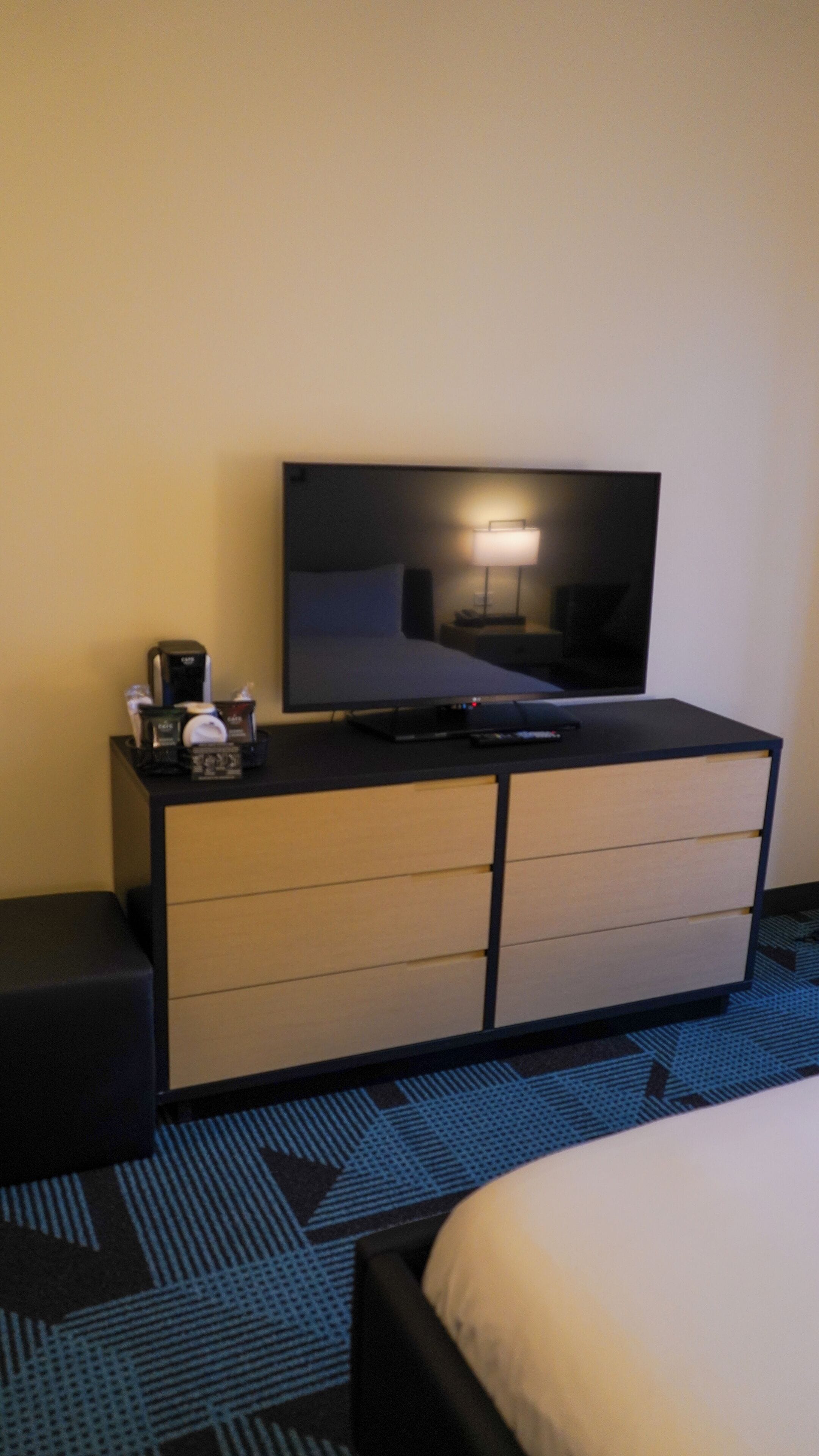 Una habitación de hotel con una cama, un televisor en una cómoda, una cafetera y una lámpara.