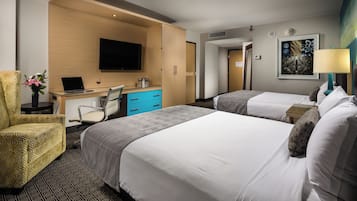Ett hotellrum med två sängar, ett skrivbord med en bärbar dator, en stol, en tv och en tavla på väggen.