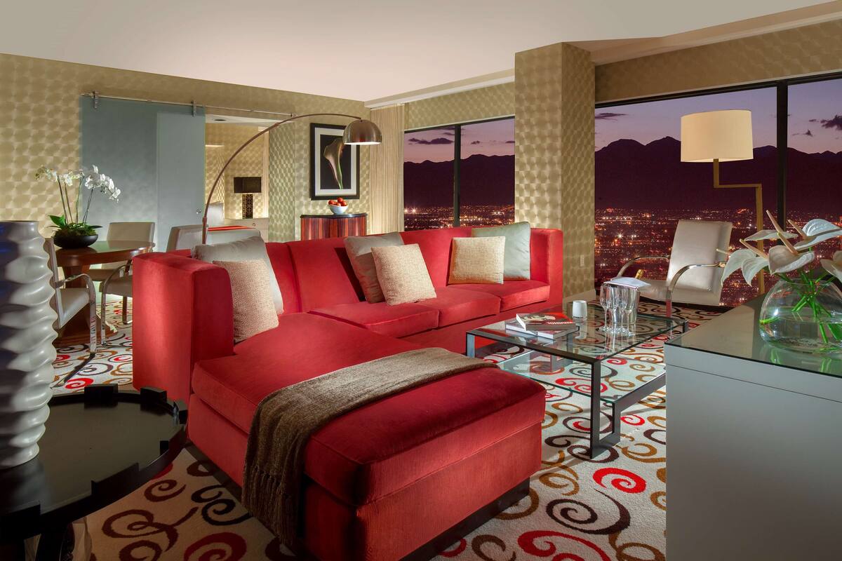 Uma sala de estar moderna com um sofá vermelho, uma mesa de centro de vidro e vista para a cidade à noite.