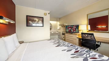 A hotel room with a bed, a desk with a computer, a TV, and a mirror.