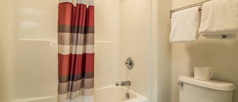 A bathroom with a bathtub, shower curtain, and a toilet.