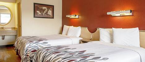 A hotel room with two beds, a bathroom with a round mirror, and a wall-mounted light fixture.