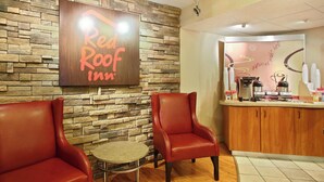 A Red Roof Inn with stone walls, leather chairs, a small round table, and a coffee station. - Red Roof Inn Greensboro Coliseum (Greensboro)